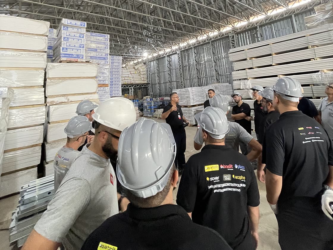 Turma de franqueados em visita técnica ao centro de distribuição do Grupo Fast, com o instrutor apresentando o estoque de perfis e placas